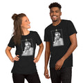Two models wearing matching dark heather gray unisex t-shirts featuring a vintage black-and-white portrait illustration of a man in a decorative ornate frame with small text beneath it. The woman on the left has her hair up and is laughing; the man on the right is smiling broadly. Both shirts appear to be the same design on a white background.