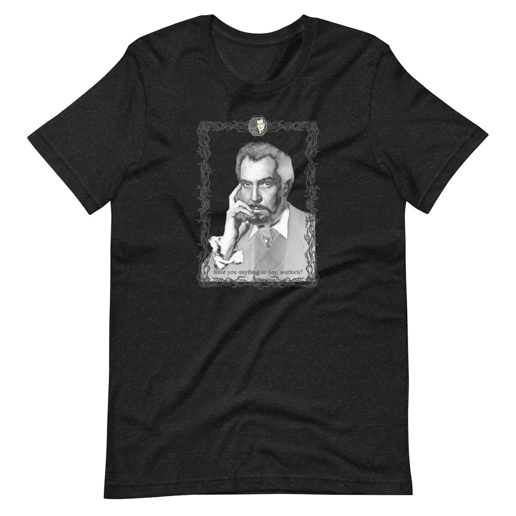 Dark heather black unisex t-shirt laid flat, featuring a black-and-white vintage portrait illustration of a distinguished older man with gray hair resting his hand against his chin, framed in an ornate decorative border with a small cameo medallion at the top. Text at the bottom of the illustration reads: "Have you anything to say, warlock?"