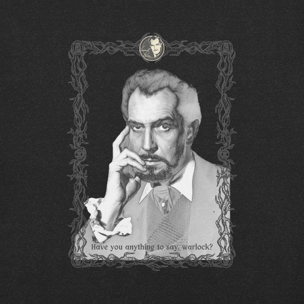 Close-up of the t-shirt graphic on a dark black fabric background: a black-and-white vintage portrait of a distinguished older man with gray hair and a goatee, resting his fingers against his cheek with an intense, brooding expression. He is dressed in a vest and open-collared shirt with ruffled cuffs. The image is framed in an ornate dark border of tangled vines and decorative scrollwork, with a small oval cameo medallion at the top. Text along the bottom reads: "Have you anything to say, warlock?"