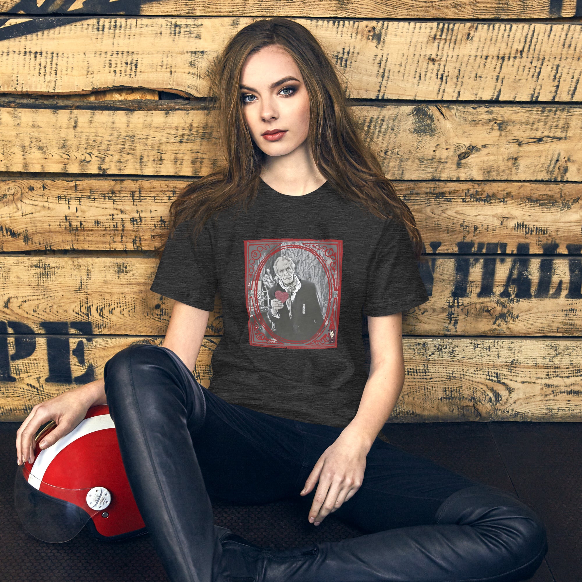 Woman wearing a black t-shirt with a graphic design, sitting against a wooden wall.