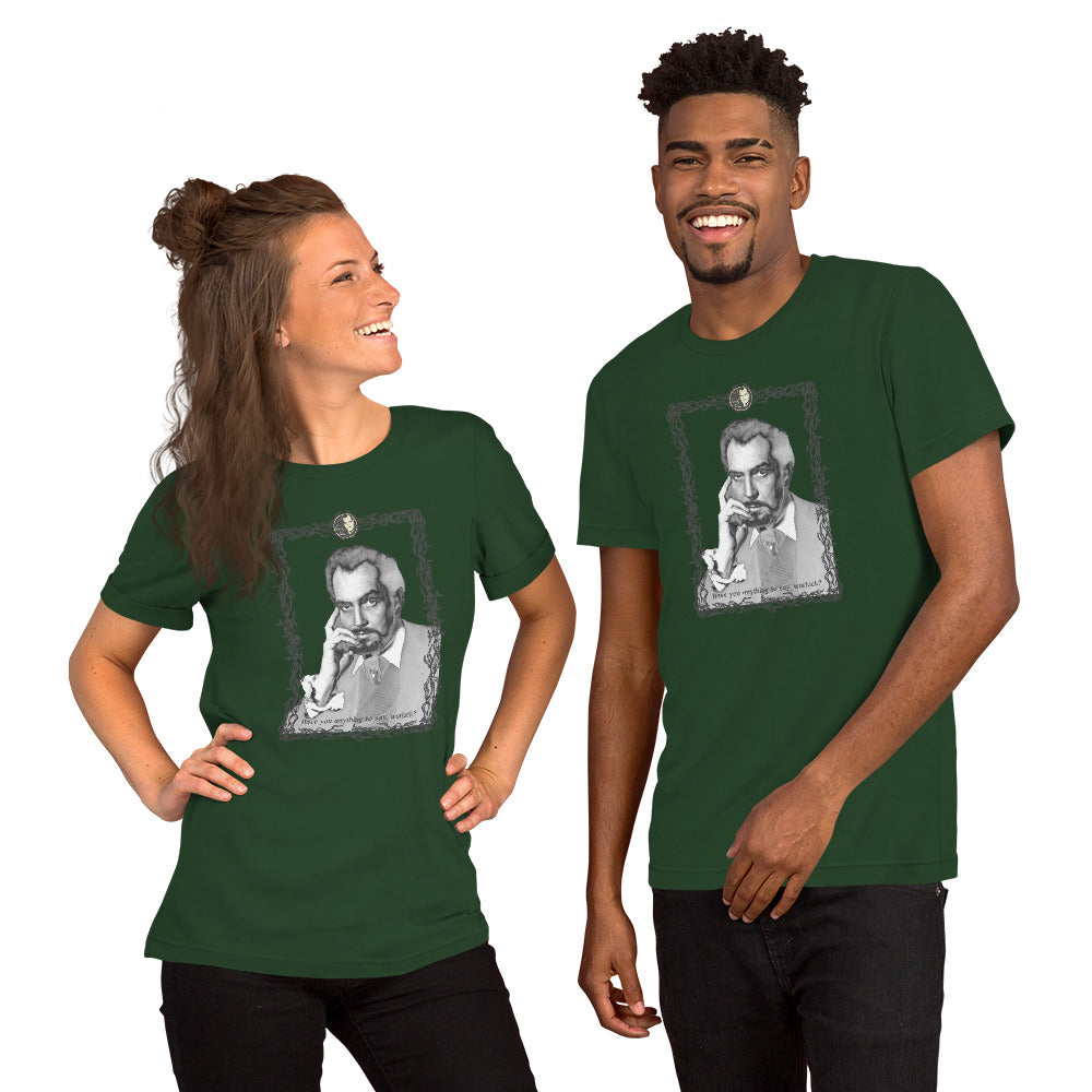 Two models wearing matching forest green unisex t-shirts featuring a black-and-white vintage portrait illustration of a distinguished older man in an ornate decorative frame with a small cameo medallion at the top and text reading "Have you anything to say, warlock?" at the bottom. The woman on the left is laughing with her hair in a half-up style; the man on the right is smiling broadly. White background.