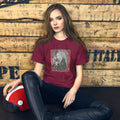 Woman wearing a maroon t-shirt with a graphic design, sitting against a wooden wall.