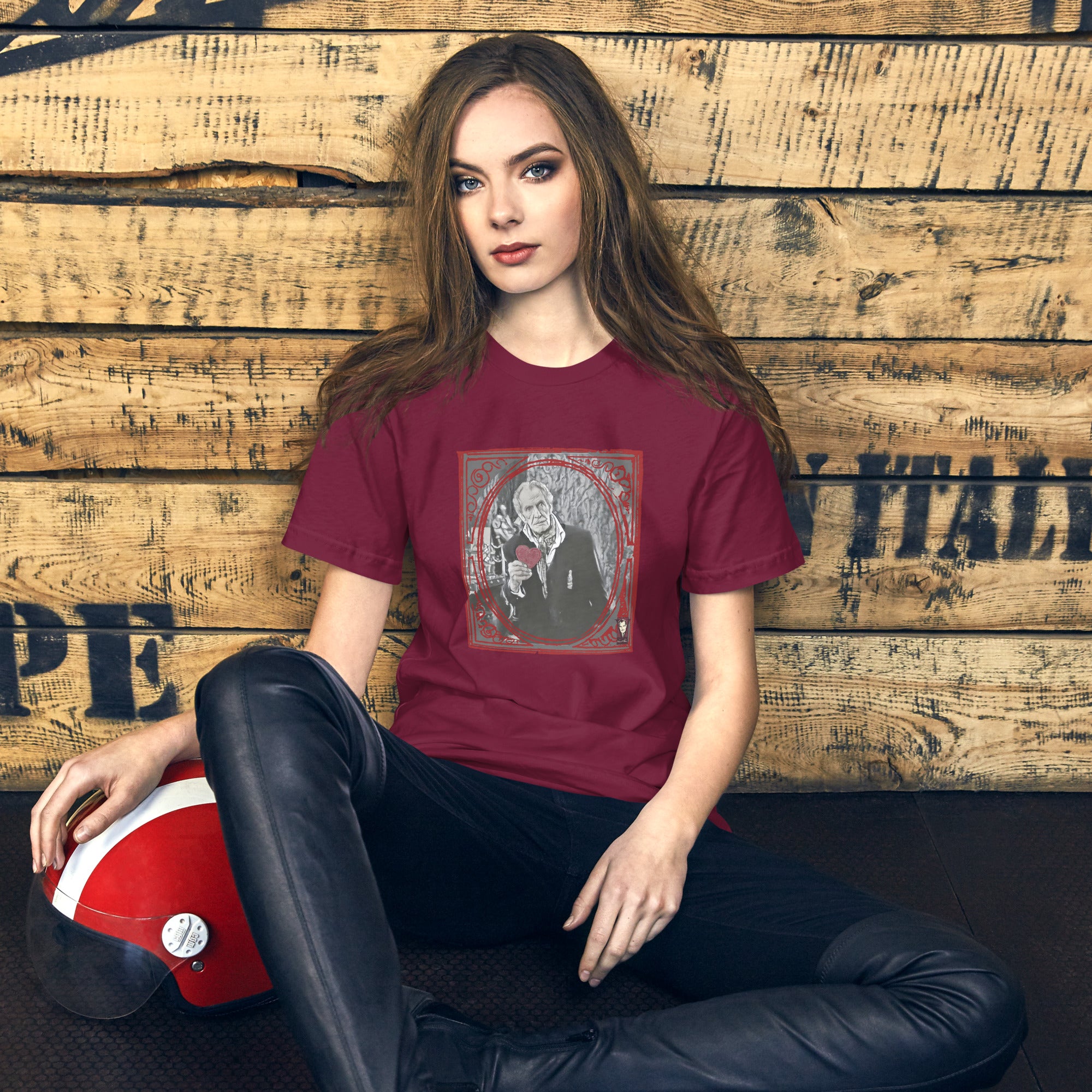 Woman wearing a maroon t-shirt with a graphic design, sitting against a wooden wall.
