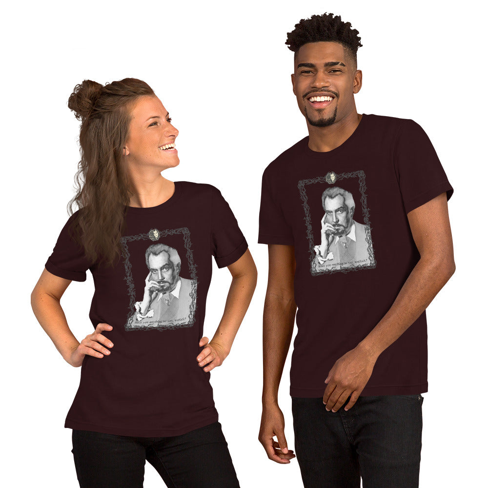 Two models wearing matching oxblood black unisex t-shirts featuring a black-and-white vintage portrait illustration of a distinguished older man in an ornate decorative frame with a small cameo medallion at the top and text reading "Have you anything to say, warlock?" at the bottom. The woman on the left is laughing and has her hair in a half-up style; the man on the right is smiling broadly. White background.