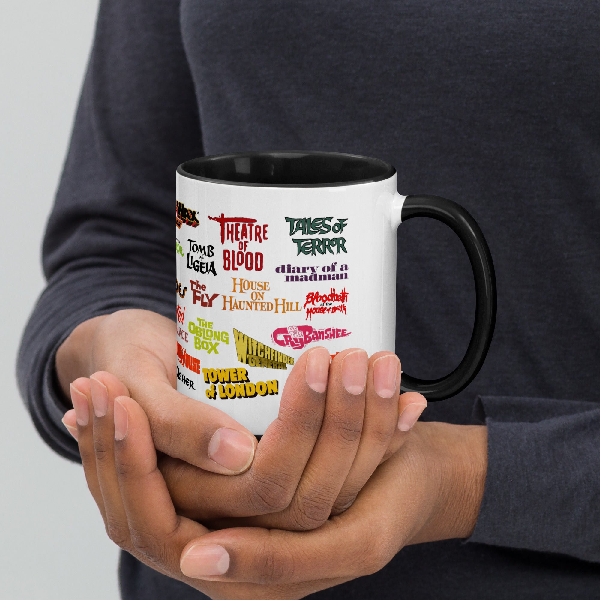 A person holding a white ceramic mug with colorful text and graphics related to classic horror and sci-fi films.